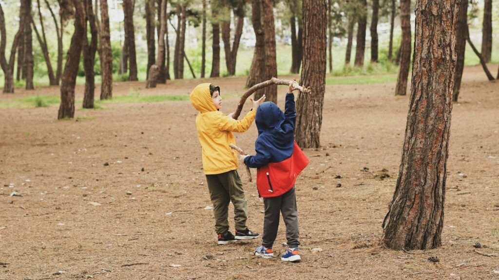 Two children exploring STEM learning while playing with a large stick in a forest.